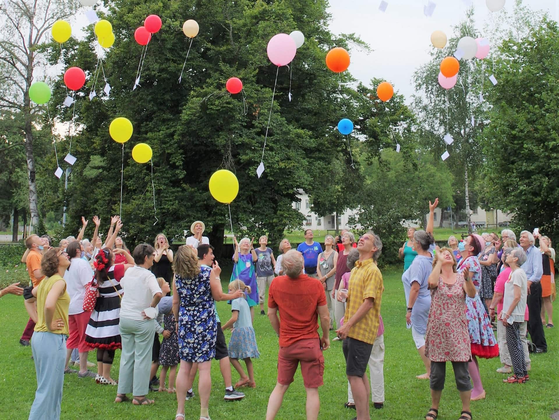 Menschen lassen bunte Luftballons in einem Park steigen.